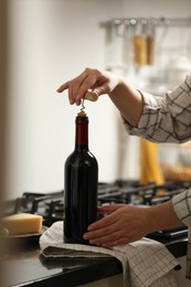 Photo of Woman opening wine bottle with corkscrew at countertop indoors, closeup