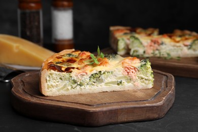 Photo of Piece of delicious homemade quiche with salmon and broccoli on black table, closeup