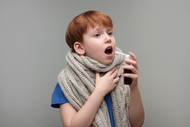 Photo of Little boy with scarf using throat spray on grey background