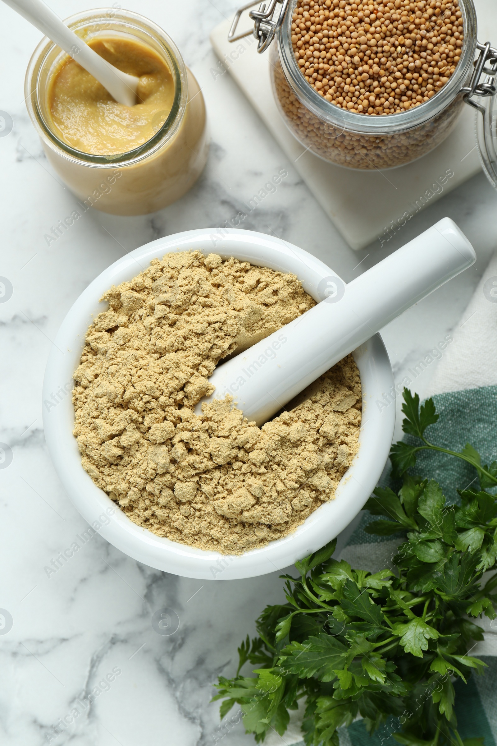 Photo of Mortar with aromatic mustard powder, grains and parsley on white marble table, flat lay