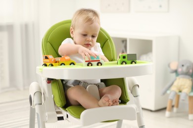 Children toys. Cute little boy playing with toy cars in high chair at home