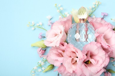 Luxury perfume and floral decor on light blue background, flat lay. Space for text