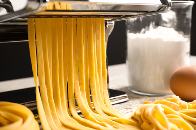 Photo of Pasta maker machine with dough and products on table, closeup