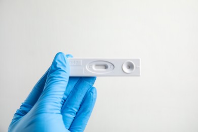 Photo of Doctor in gloves holding disposable express test for hepatitis on white background, closeup