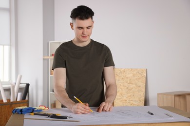 Young handyman working with blueprints at table in room