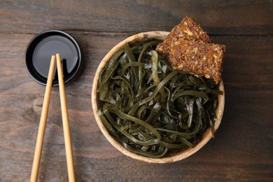 Photo of Tasty seaweed salad in bowl served on wooden table, flat lay