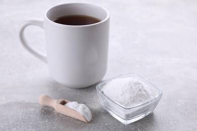 Photo of Bowl and scoop of sweet fructose powder near cup with tea on light grey table