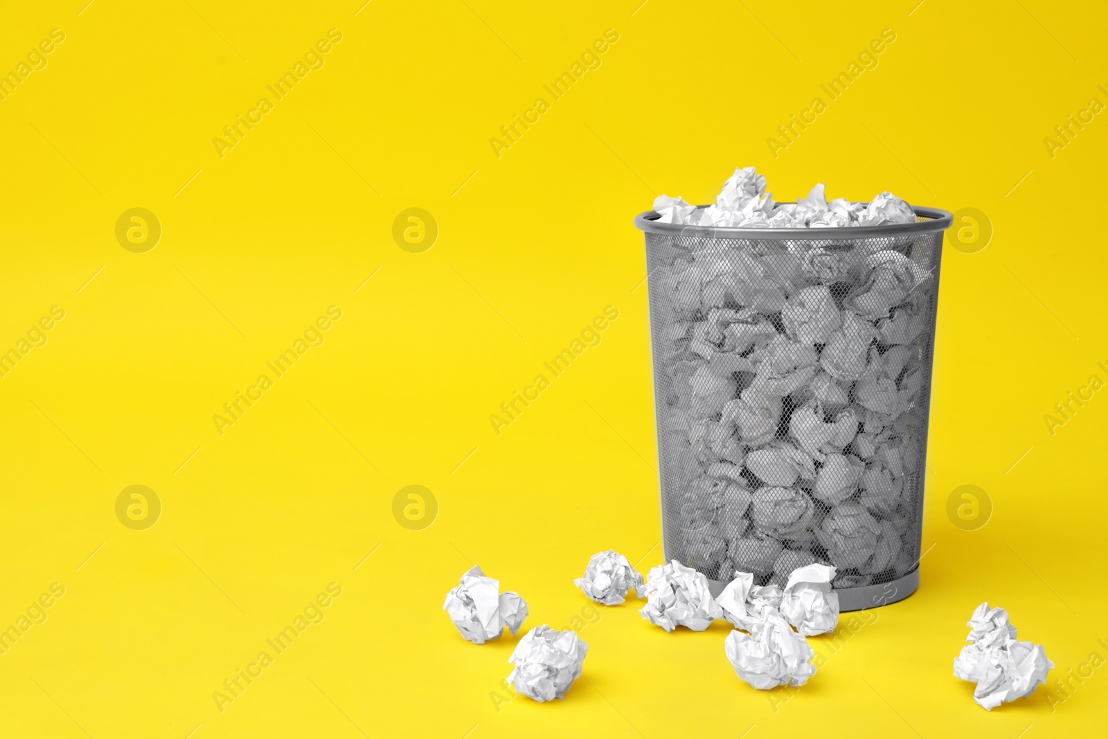 Photo of Metal bin with crumpled paper on color background, space for text