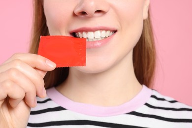 Photo of Woman holding condom on pink background, closeup. Safe sex