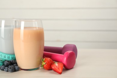 Tasty shakes with berries, dumbbells and measuring tape on wooden table, space for text. Weight loss