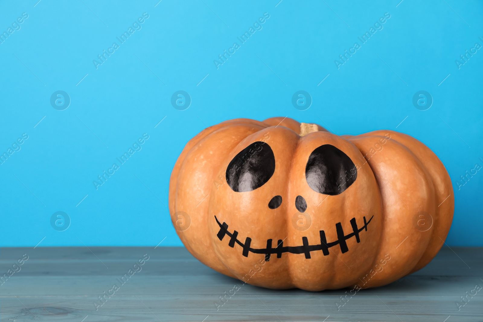 Photo of Pumpkin with drawn spooky face on light blue background, space for text. Halloween celebration