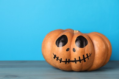 Photo of Pumpkin with drawn spooky face on light blue background, space for text. Halloween celebration
