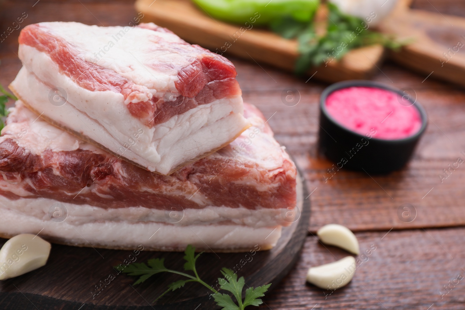 Photo of Pieces of tasty pork fatback with garlic and parsley on wooden table, closeup