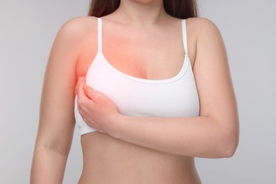 Young woman suffering from breast pain on light grey background, closeup