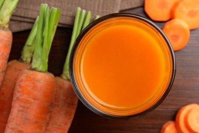 Photo of Glass of tasty juice and fresh carrot on wooden table, flat lay