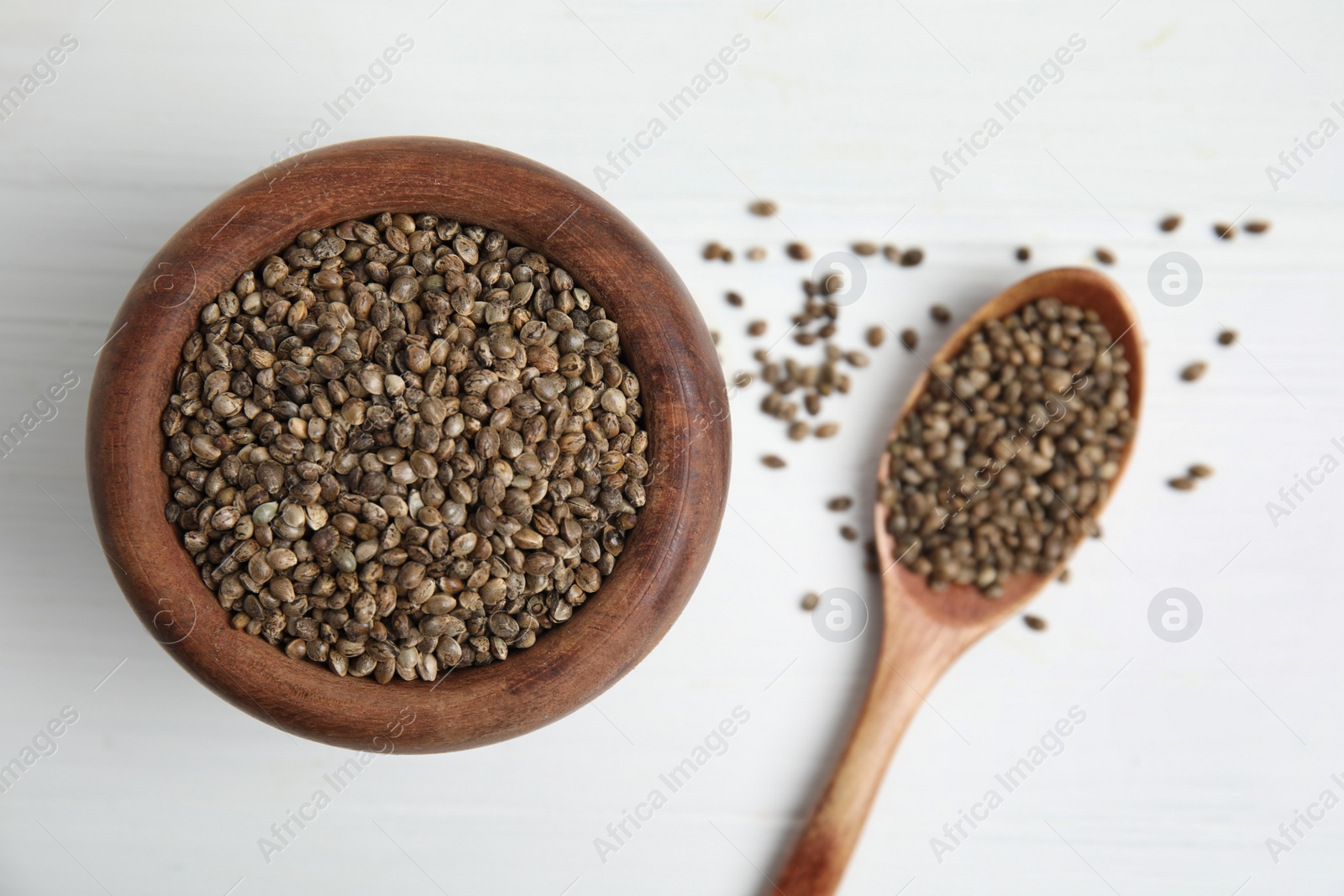 Photo of Wooden bowl and spoon with organic hemp seeds on white table, flat lay