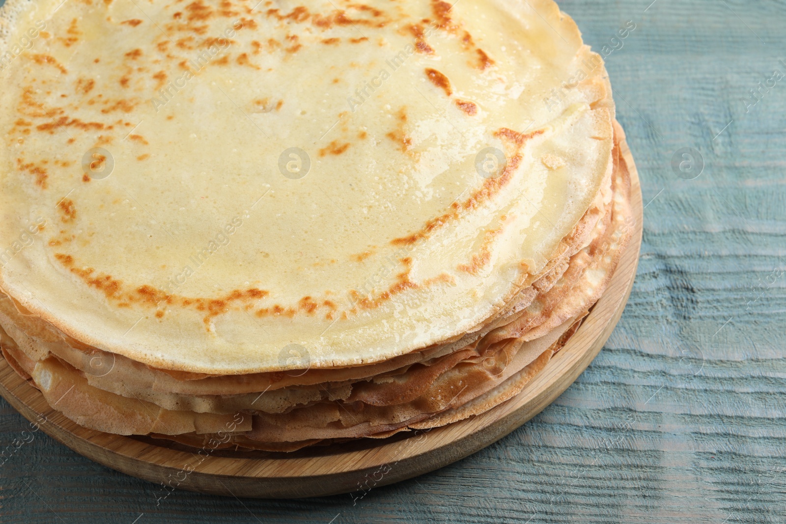 Photo of Stack of delicious crepes on blue wooden table, closeup