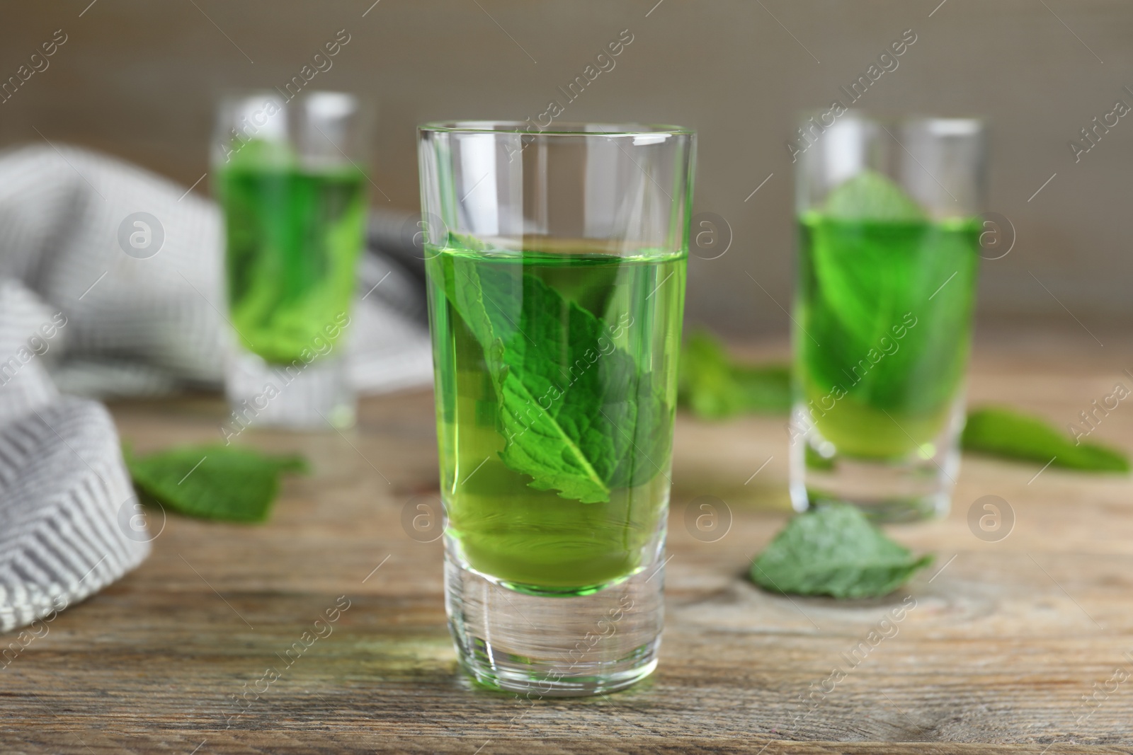 Photo of Delicious mint liqueur with green leaves on wooden table