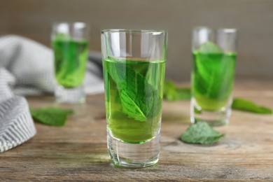 Photo of Delicious mint liqueur with green leaves on wooden table