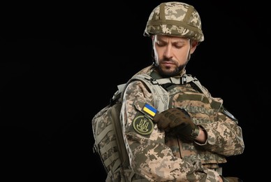 Soldier with Ukrainian flag and trident on military uniform against black background. Space for text