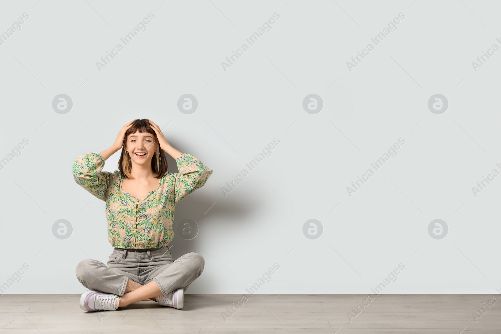 Photo of Happy young girl sitting on floor near white wall. Space for text