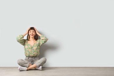 Happy young girl sitting on floor near white wall. Space for text