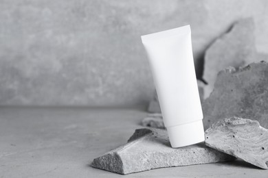 Photo of Tube of hand cream among stones on grey background. Mockup for design