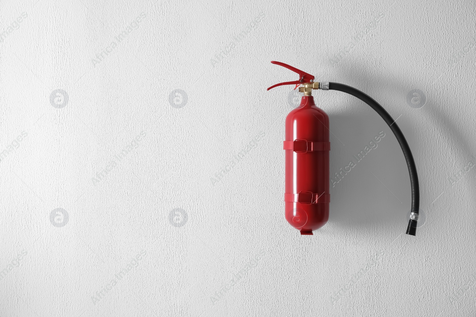 Photo of Fire extinguisher hanging on white wall. Space for text