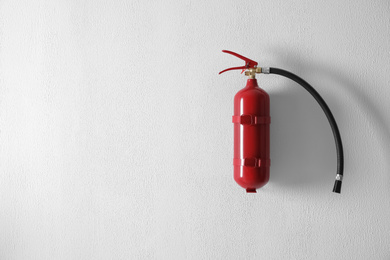 Photo of Fire extinguisher hanging on white wall. Space for text