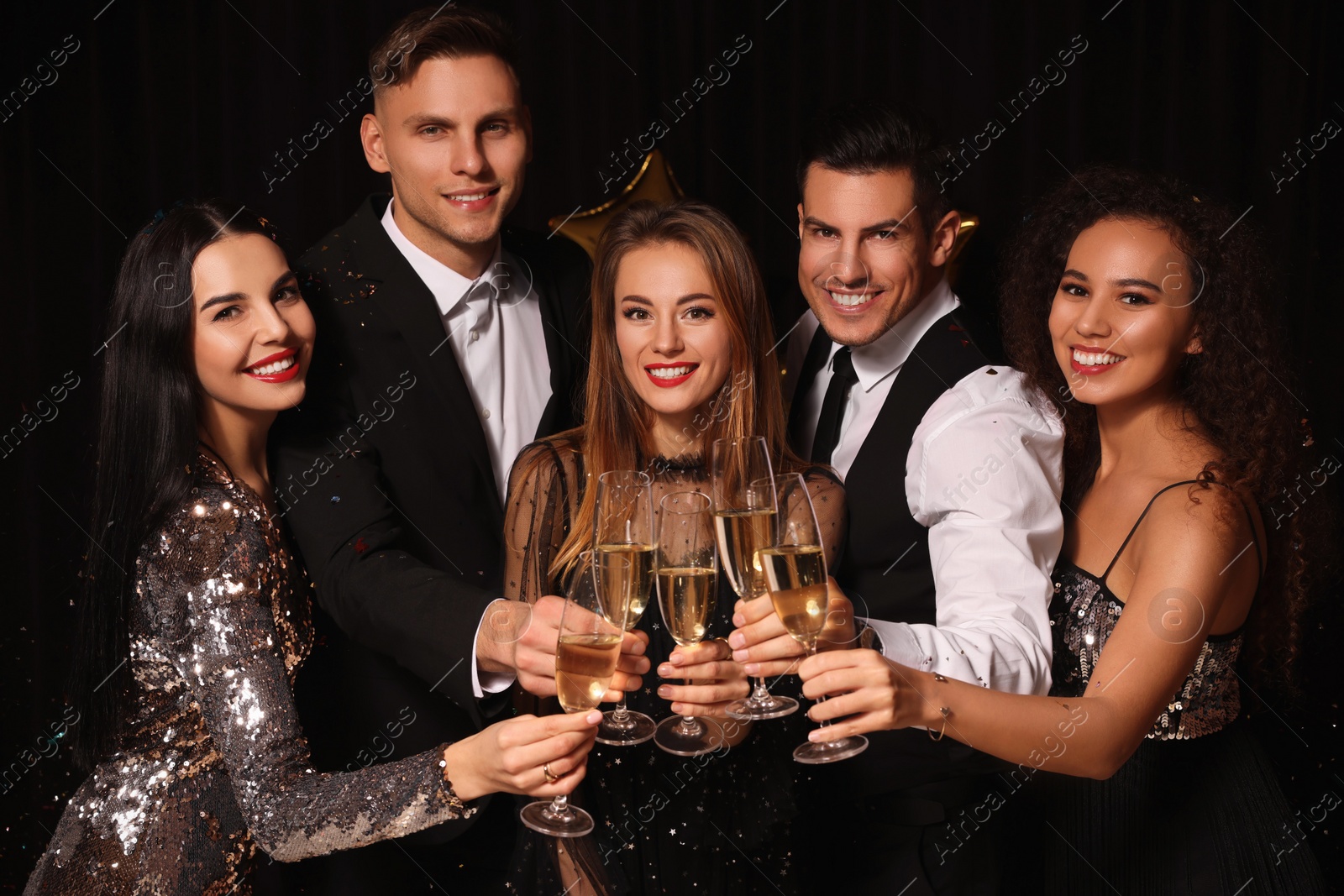 Photo of Happy friends with glasses of sparkling wine celebrating New Year on black background