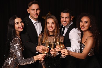 Photo of Happy friends with glasses of sparkling wine celebrating New Year on black background