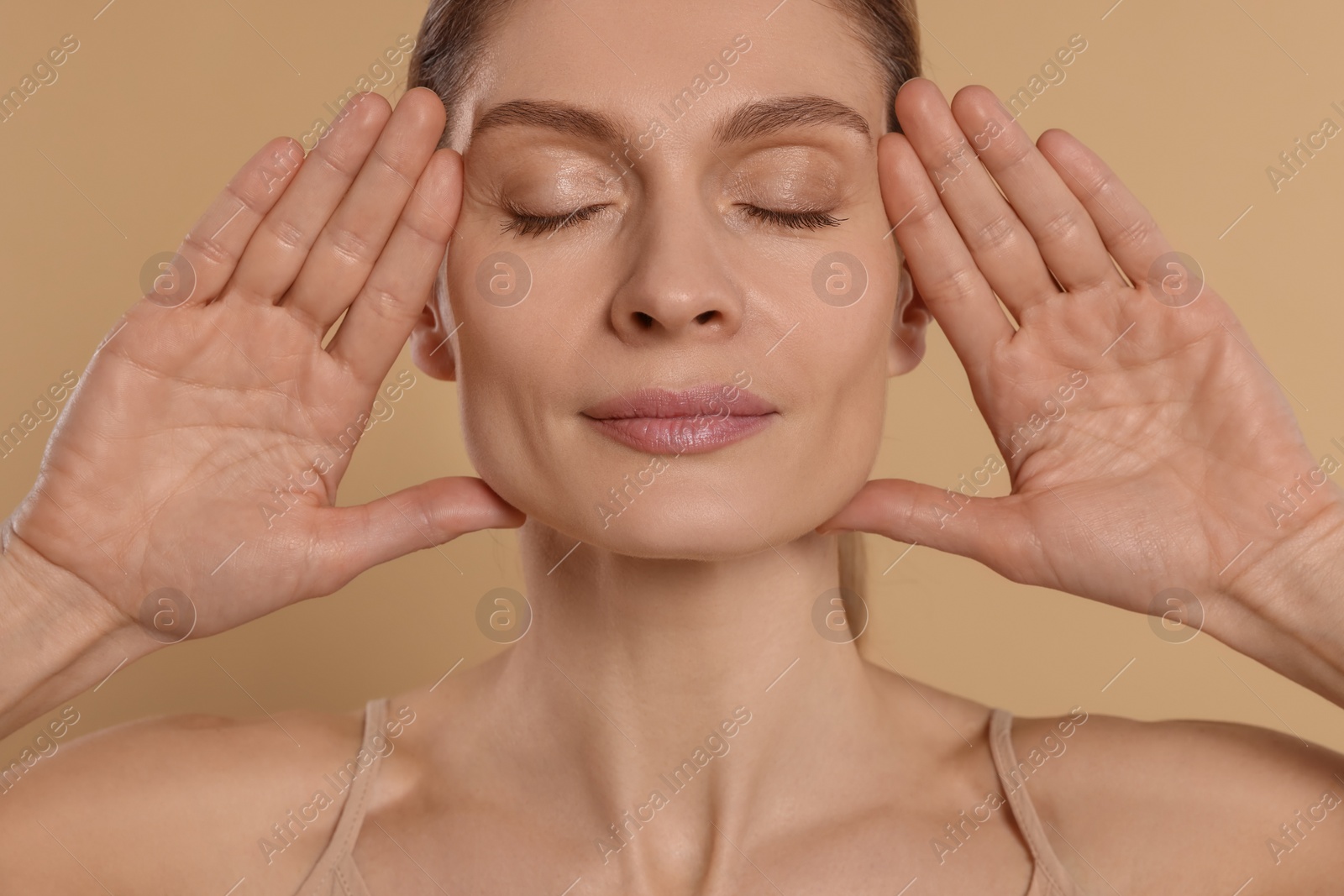 Photo of Woman massaging her face on beige background