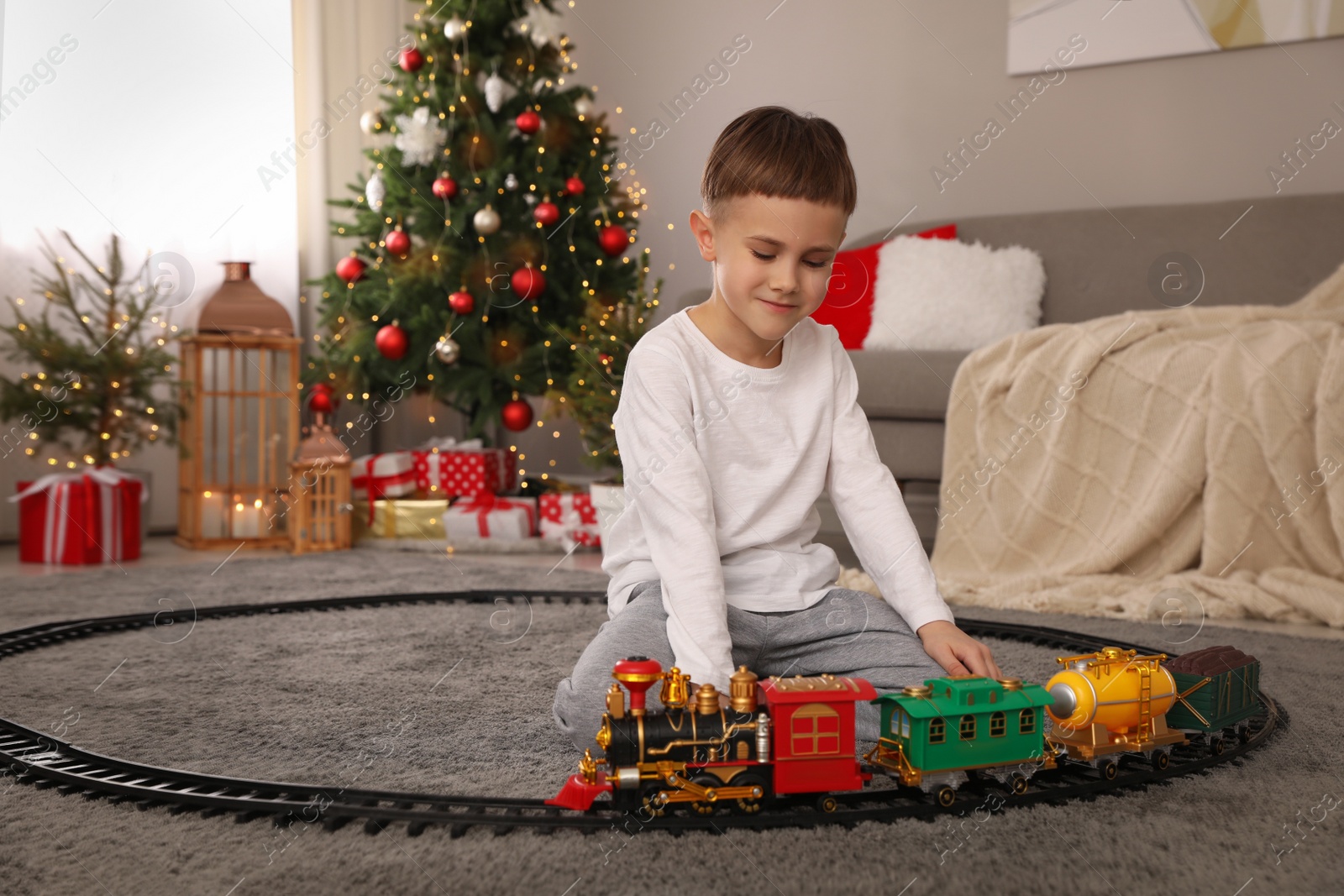 Photo of Little boy playing with colorful train toy in room decorated for Christmas