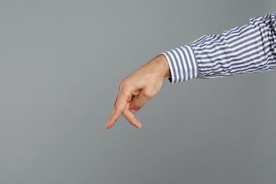 Photo of Man imitating walk with hand on grey background, closeup. Finger gesture