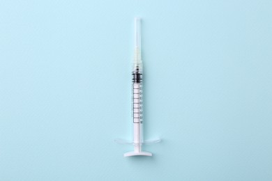 Cosmetology. Medical syringe on light blue background, top view