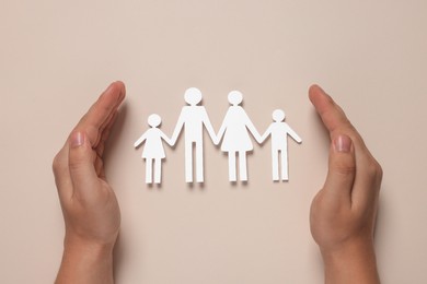 Photo of Man protecting paper family figures on beige background, top view. Insurance concept