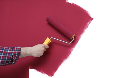 Man applying burgundy paint with roller brush on white wall, closeup