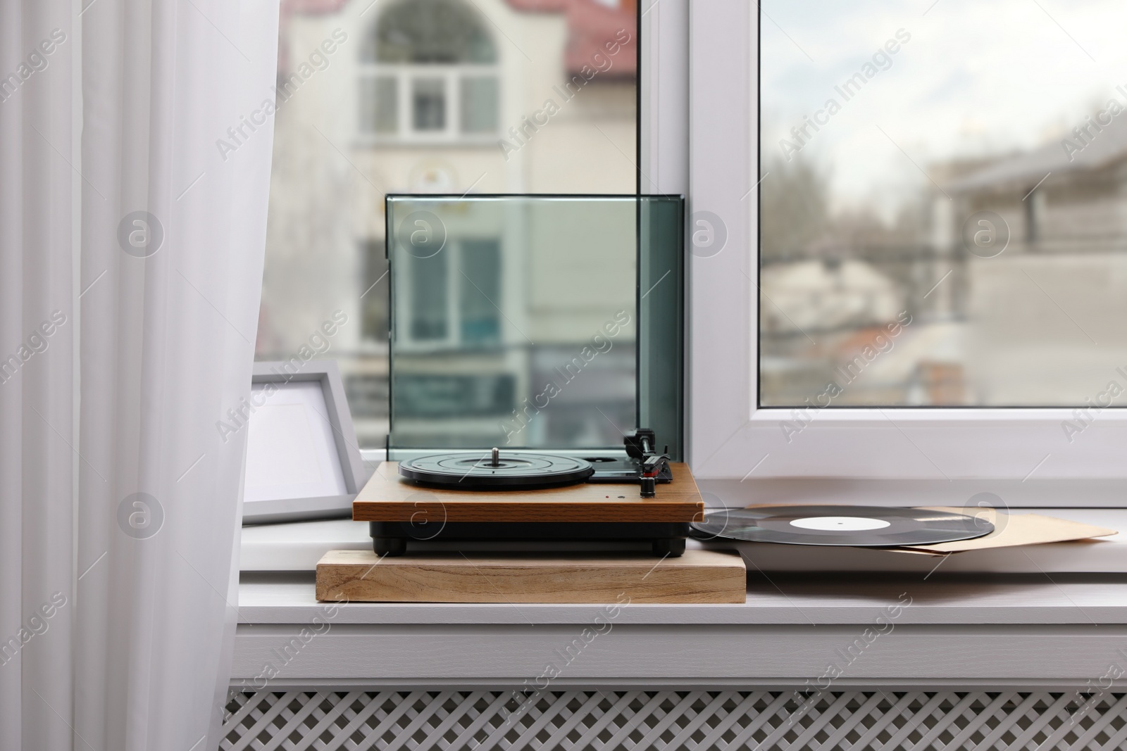 Photo of Stylish turntable with vinyl discs on windowsill in room