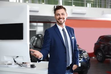 Salesman standing in modern auto dealership. Buying new car