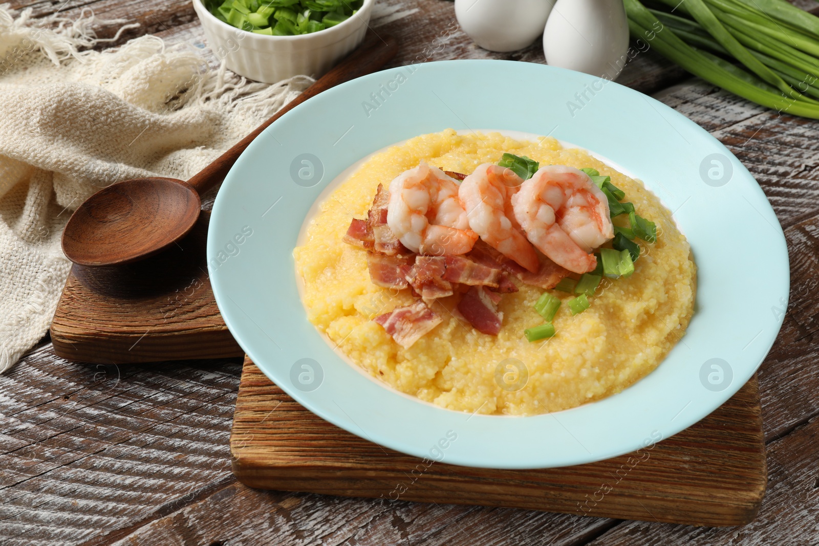 Photo of Plate with fresh tasty shrimps, bacon, grits and green onion on wooden table