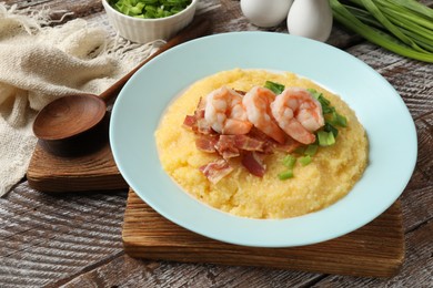 Photo of Plate with fresh tasty shrimps, bacon, grits and green onion on wooden table