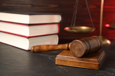 Photo of Wooden gavel, scales and stack of books on dark textured table, closeup