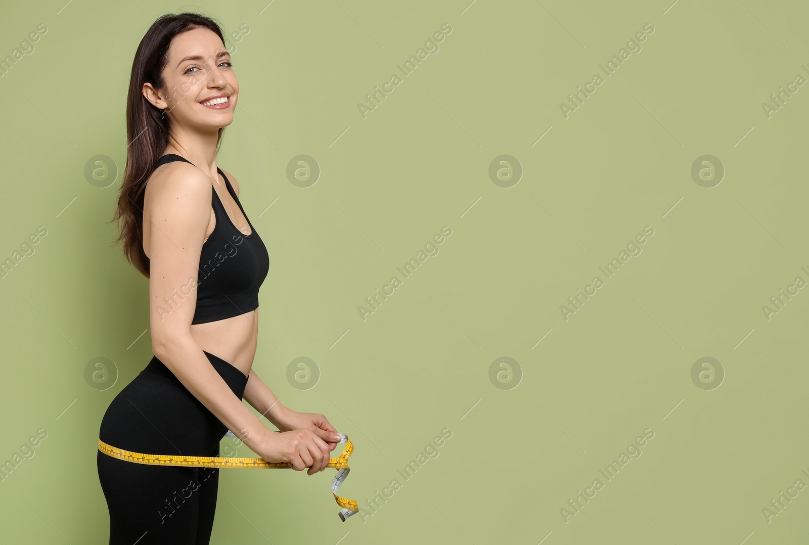 Photo of Happy young woman with measuring tape showing her slim body on green background, space for text