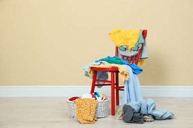 Photo of Different clothes, red chair and wicker basket near beige wall, space for text