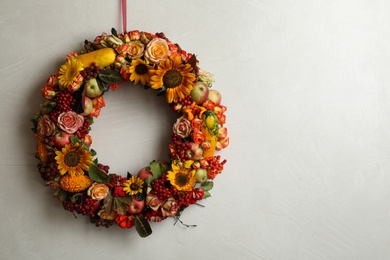 Photo of Beautiful autumnal wreath with flowers, berries and fruits hanging on light grey background. Space for text