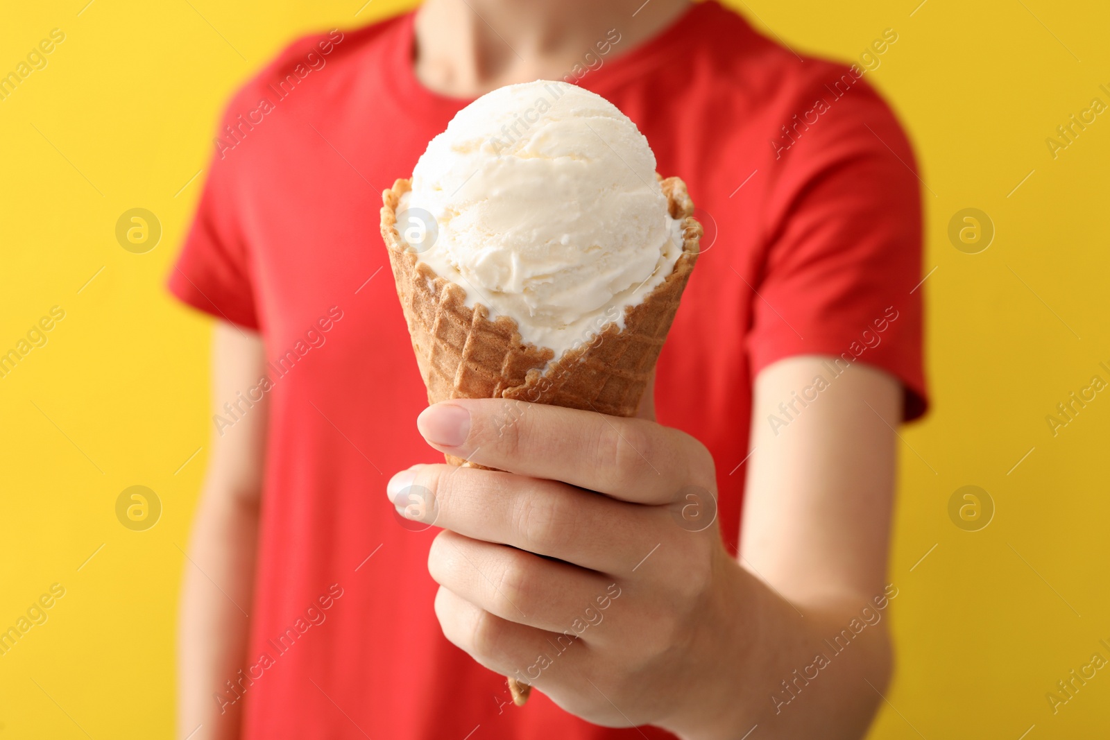 Photo of Woman holding white ice cream in wafer cone on yellow background, closeup