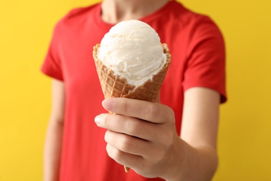 Woman holding white ice cream in wafer cone on yellow background, closeup