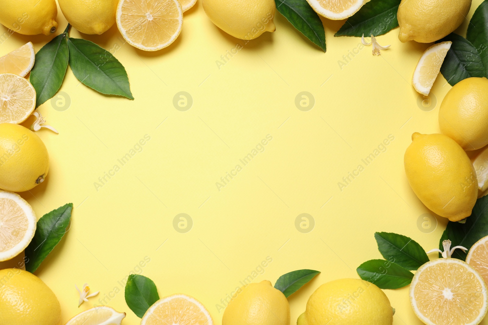 Photo of Frame made of fresh ripe lemons and green leaves on yellow background, top view. Space for text