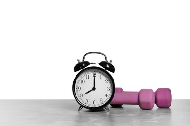 Photo of Alarm clock and dumbbells on marble table against grey background, space for text. Morning exercise