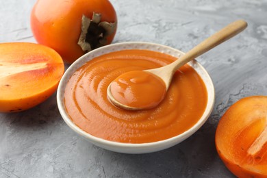 Photo of Delicious persimmon jam and fresh fruits on grey table